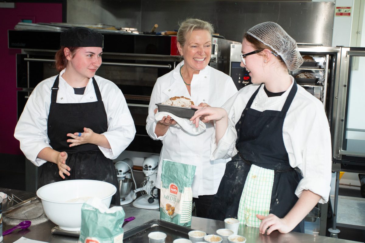 Three cooks in a kitchen check a loaf of bread.